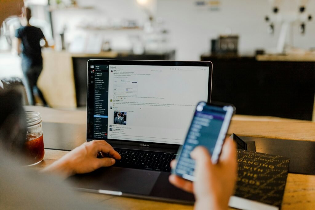 A person holding a phone beside an open laptop in a quiet room